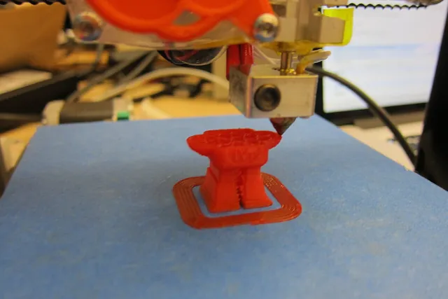 A desktop 3D printer forming a small red model.