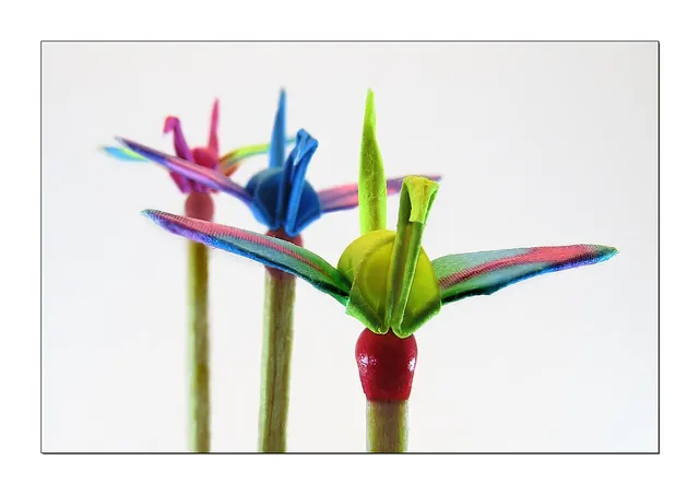 Tiny folded paper cranes balanced on match heads.