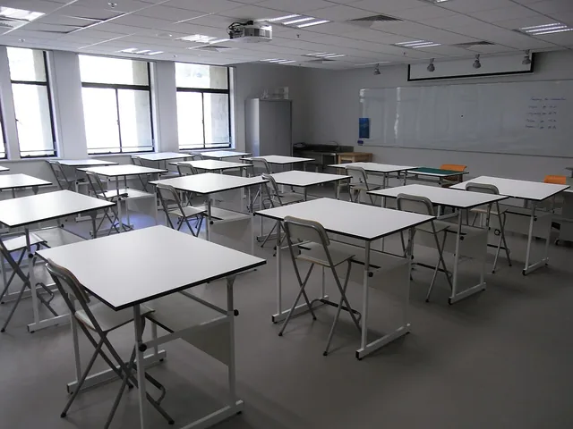 An empty classroom arranged with worktables, tall chairs and a whiteboard.