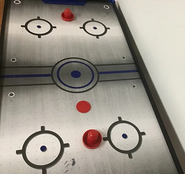 Red paddles and a puck resting on an air hockey table.