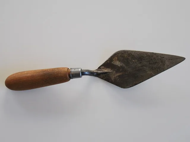 An archaeological trowel with a wooden handle and pointed steel blade.