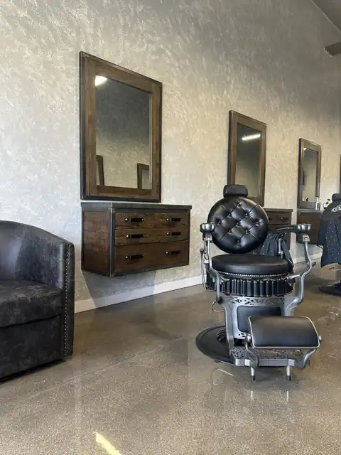 An empty barber chair facing mirrors and wooden drawers.