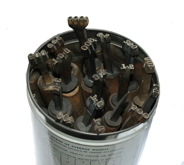 Brass numbering and lettering tools stored upright in a round tin.