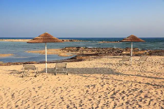 Sun loungers and thatched parasols on a sandy beach beside the sea.