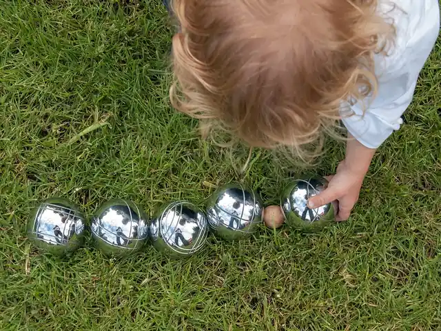Metal pétanque balls and a small wooden jack arranged on grass.