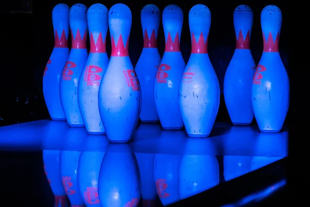 Bowling pins illuminated by blue lighting at the end of a lane.