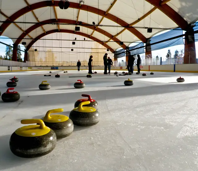 Curling stones with yellow and red handles on an indoor sheet of ice.