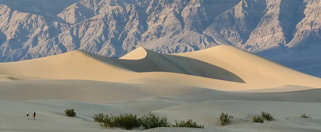 Sunlight and shadow across sand dunes beneath rocky mountains.