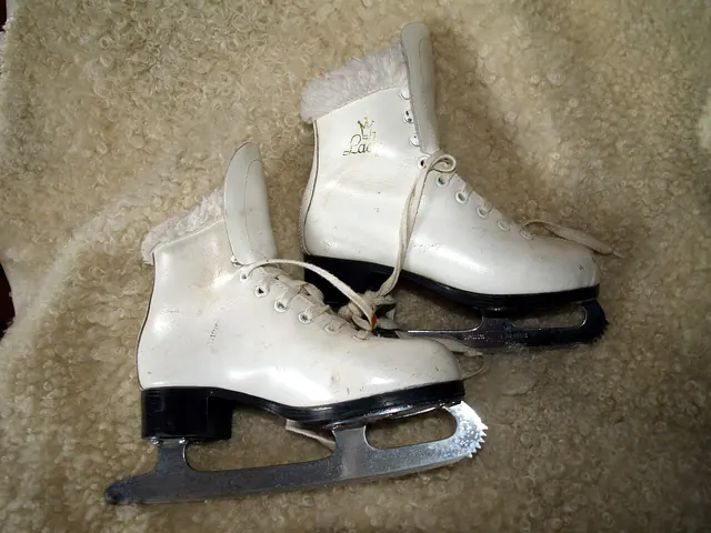 A pair of white figure skates with laces and steel blades.