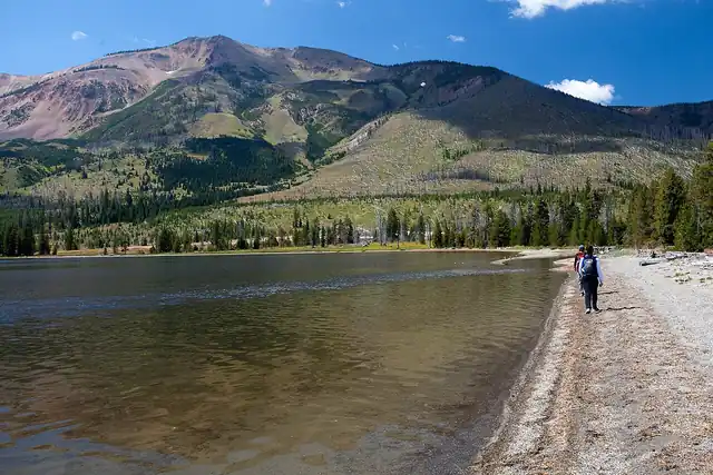 Clear water along a mountain lake with a wooded slope beyond.