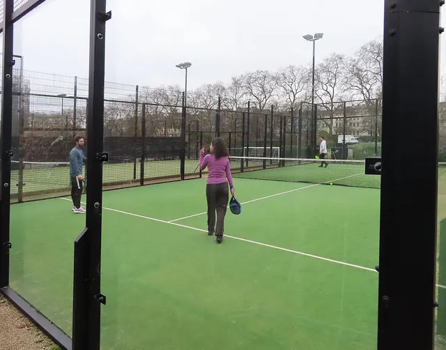 Players holding padel rackets on an enclosed outdoor court.