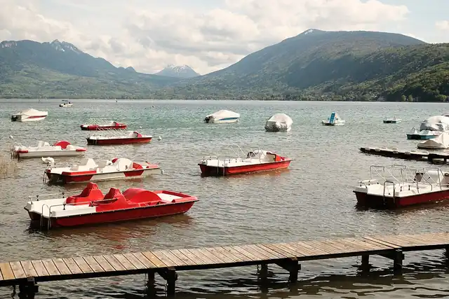 Red and white pedal boats moored beside a lake with mountains beyond.
