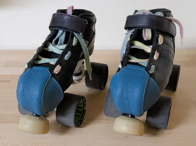 A pair of black quad roller skates with blue toe covers.