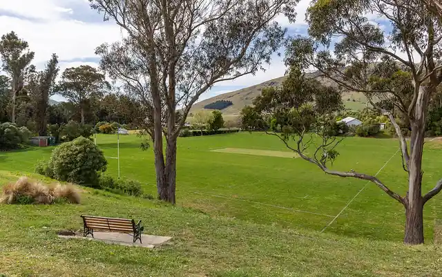 An empty grass rugby pitch surrounded by trees and hills.
