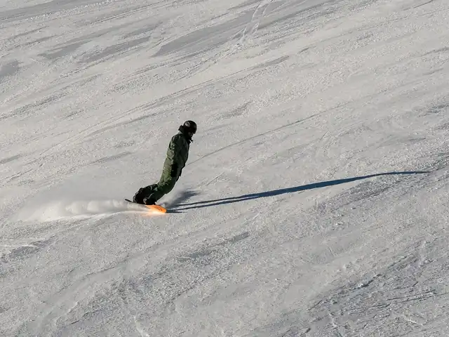 A snowboarder carving across a snowy slope and casting a long shadow.