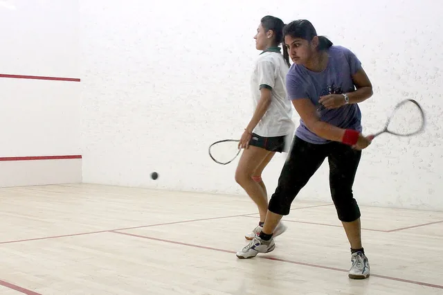 Two players with rackets during a game on an indoor squash court.