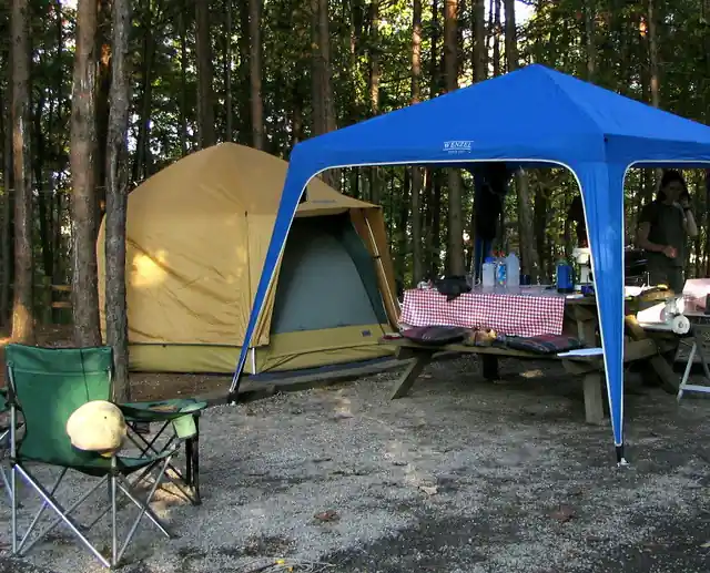 A camping tent, gazebo and folding chairs set up among trees.