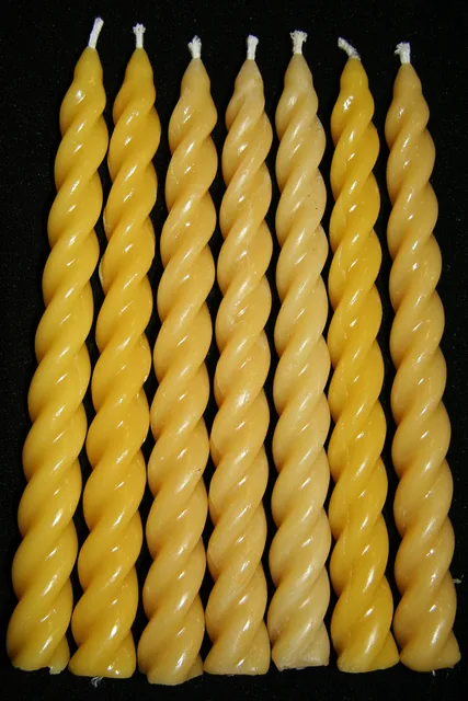 Seven twisted beeswax candles with unlit wicks against a dark background.