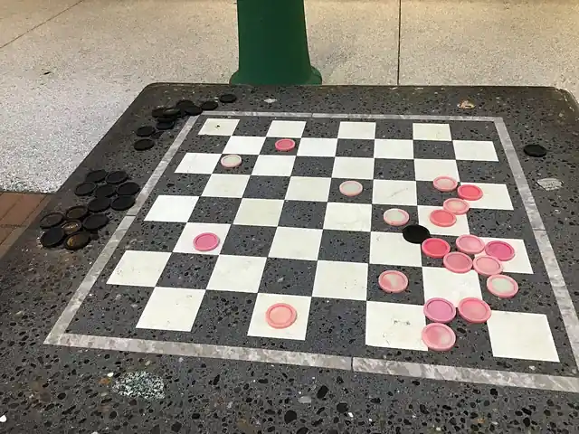 Black and red checkers placed on an outdoor game table.