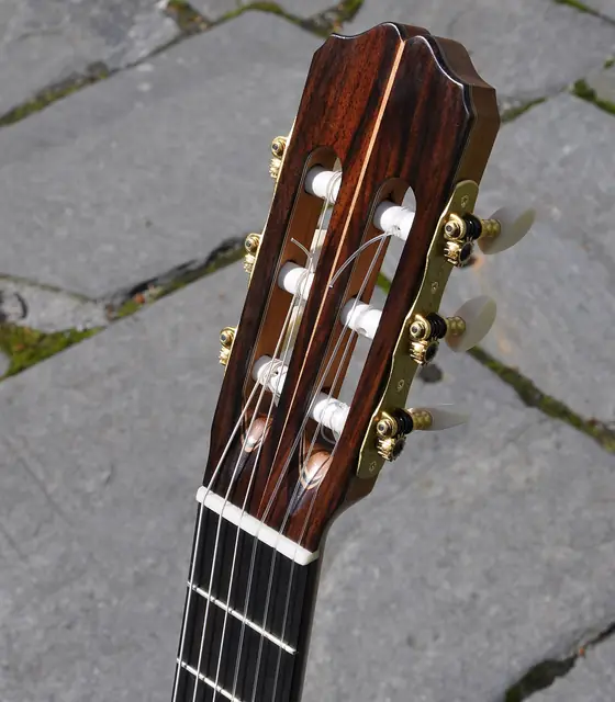 The wooden headstock, strings and tuning pegs of a classical guitar.