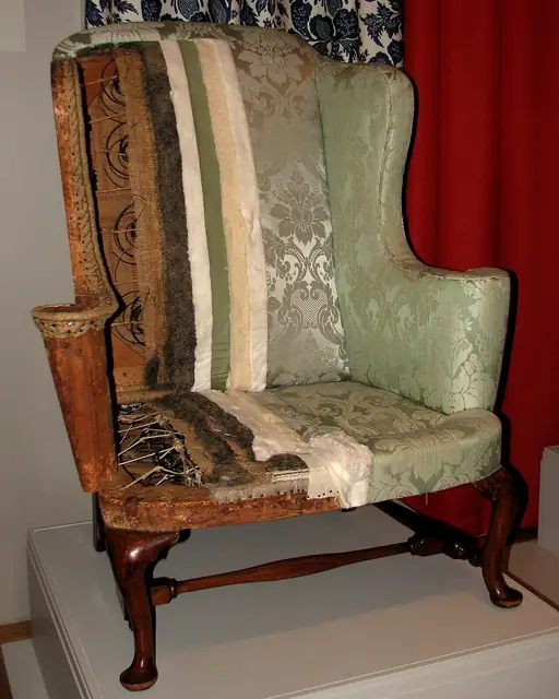 A partly uncovered chair showing its wooden frame and upholstery.