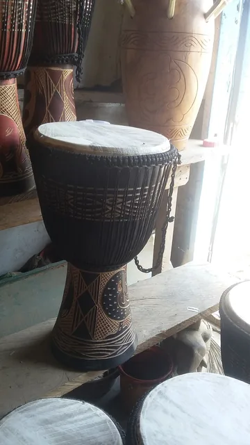 A djembe drum with a carved wooden body displayed among other drums.