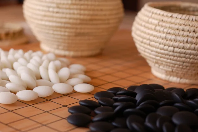 Black and white Go stones beside woven bowls on a wooden board.