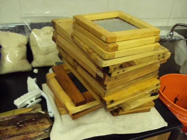 Wooden moulds and deckles stacked in a papermaking workshop.