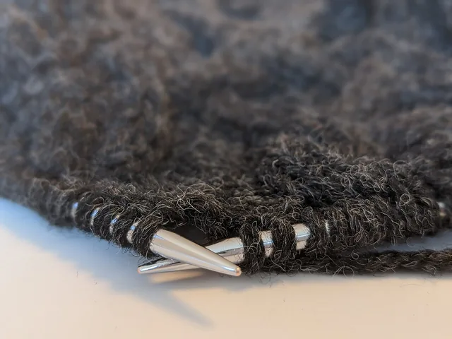 Knitting needles holding loops of dark wool yarn in an unfinished piece.