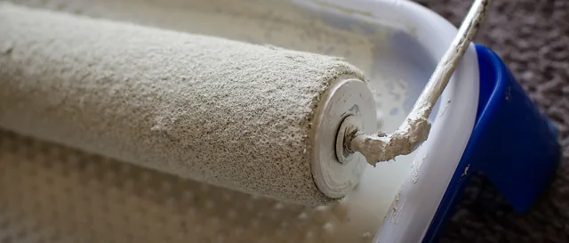 A paint roller coated in white paint above an open paint container.