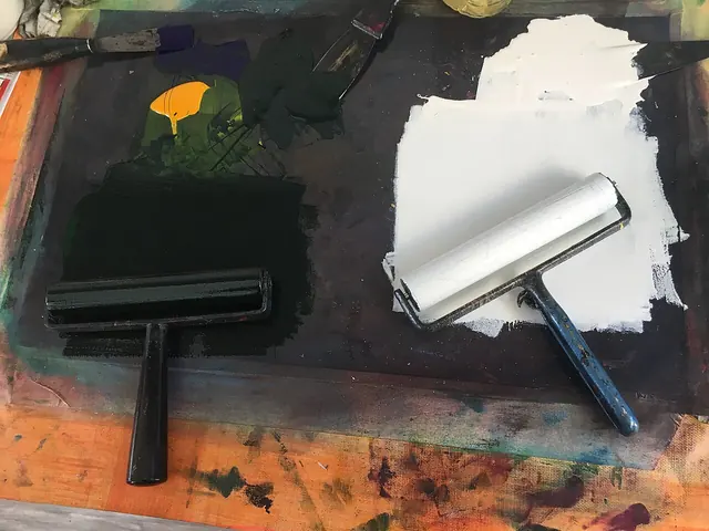 Printmaking rollers beside black and white ink on a work surface.