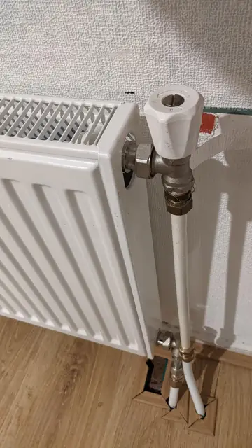 A white panel radiator with its valve and pipes visible.