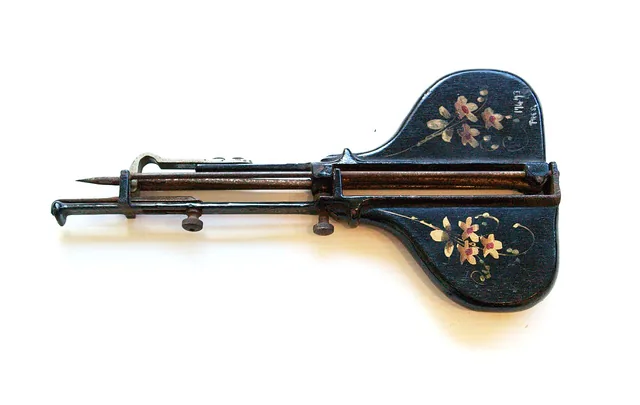 An antique rug-hooking tool with a metal needle mechanism and floral decoration.