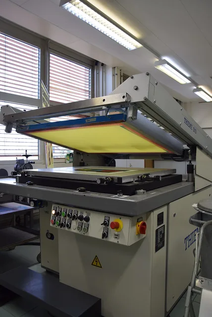 An open screen-printing press with a yellow mesh screen in a workshop.