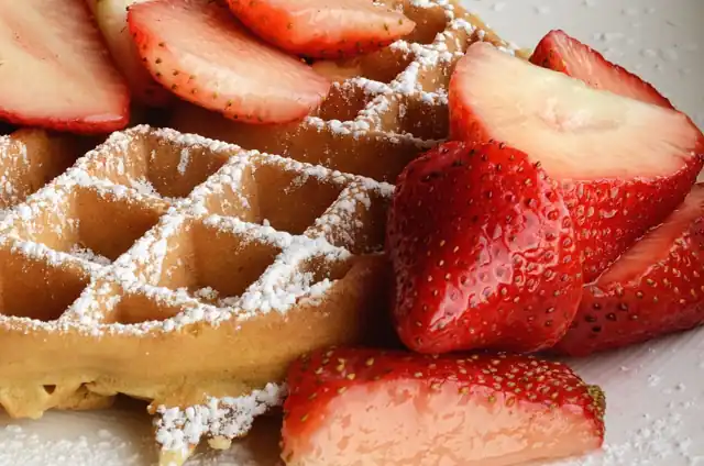 A waffle topped with fresh strawberries and powdered sugar.