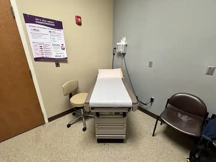 A medical examination table beside a visitor chair.