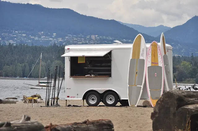 Stand-up paddleboards beside a rental trailer at a beach.